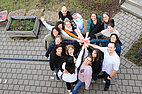 Foto vom Team der Campus-Kita von oben fotografiert, die Mitarbeiter*innen stehen im Kreis und halten ihre Hände in die Mitte 