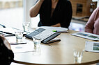 Team-Besprechungen haben wir in allen Bereichen, egal ob Büroangestellte, Köche, Hausmeister oder Kita Mitarbeiter*innen. Foto auf dem man einen runden Tisch mit Papieren, Gläsern und einen Kalender sieht und man erkennt, dass Personen an dem Tisch sitzen