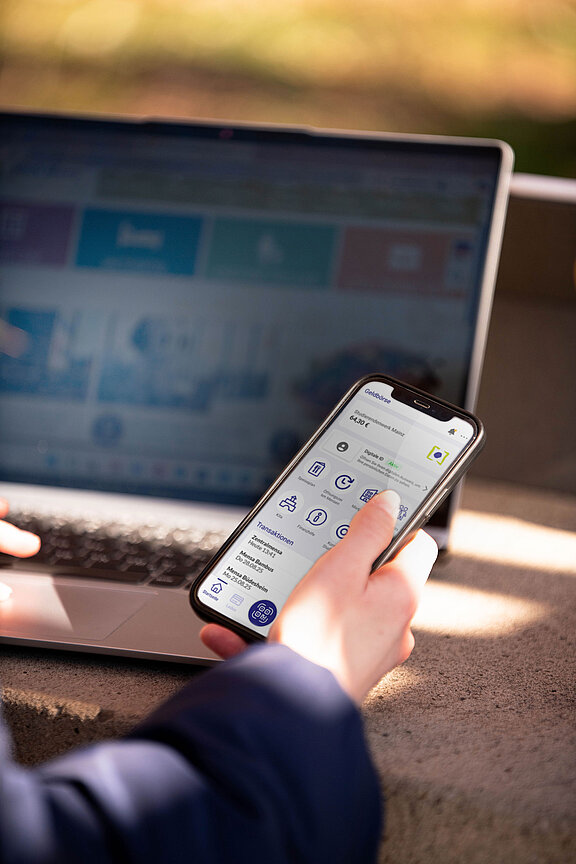 Foto of a hand holding a mobile phone with the studiwerkmainz app seen on the display